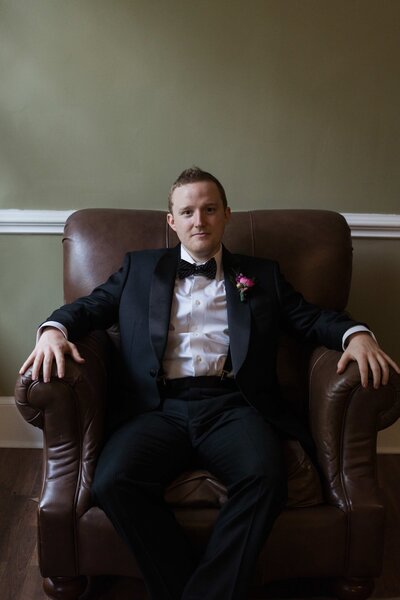 groom sits in brown leather chair in charlotte