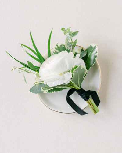 This detailed layflat photograph captures the groom's boutonniere in a close-up shot, showcasing its elegant design. The refined floral arrangement adds a touch of sophistication to the wedding day, emphasizing the attention to detail in the groom's attire.