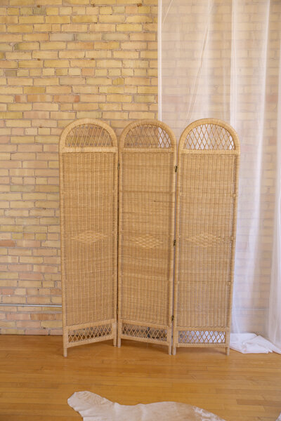 A three section rattan divider standing up in front of a brick wall.
