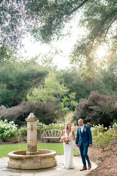 Bride and groom walking next to fountain on their wedding day at Vista Valley Country Club wedding venue