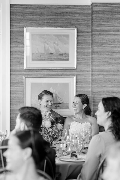 Couple laughing during rehearsal dinner speeches at the American Yacht Club