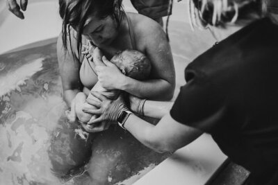 New mother cradling newborn in a birthing pool with assistance