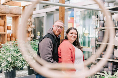 Husband stands behind wife with his arms around her.