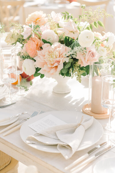 Wedding reception table close up, white table, white dishes and cutlery, and pink and white flowers in a short vase