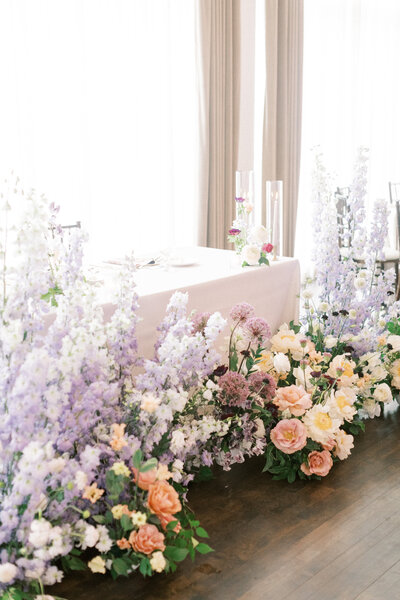 Sweetheart table at wedding decorated with peach and purple flowers.