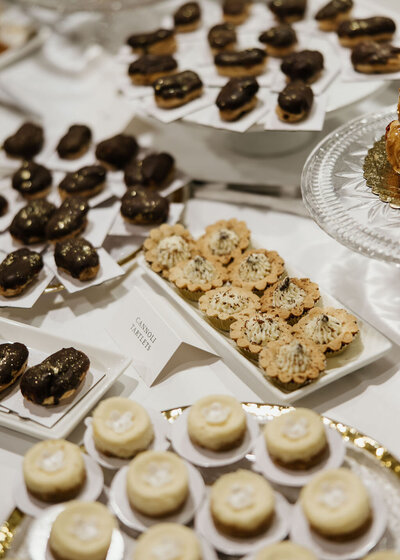 Wedding dessert bar with mini eclairs, cannoli tartlets, cheesecakes