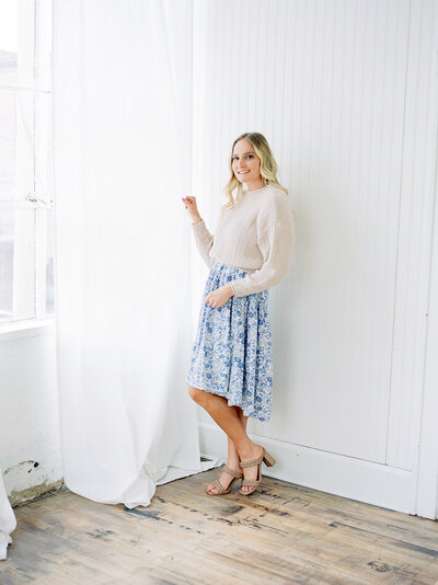 woman in floral skirt beside curtain