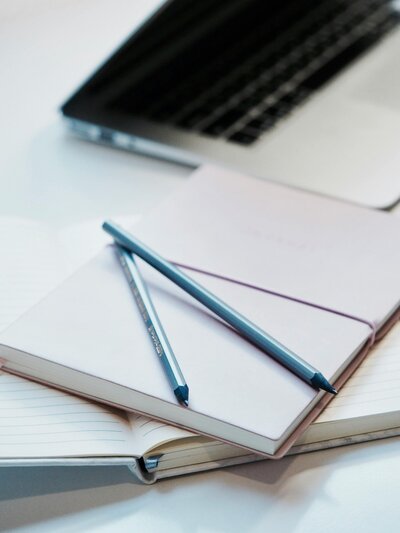 Get College-Ready This Summer with two notebooks and two pencils on a desk beside a partially visible laptop—perfect tools for The Summer Jumpstart with Mya Andersen.