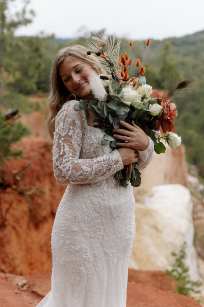 Adventurous wedding photographer captures bride smiling softly while holding her boho flower bouquet. 