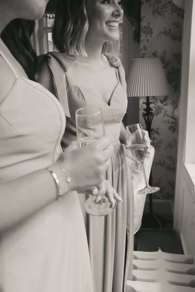 Bridesmaids holding champagne glasses looking out the window at a wedding in Canton Massachusetts. Photography by Rhode Tripper Photography