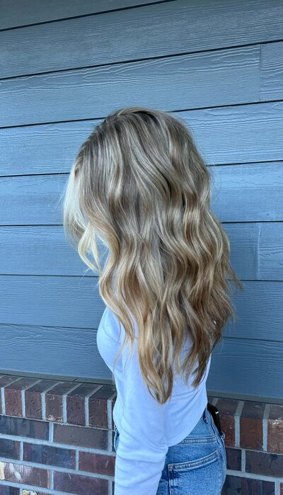 Long blonde extensions with soft beachy curls—showcasing hand-tied extension services.