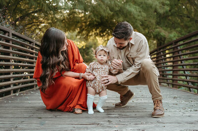 Charlotte family photographer Tonya Cassibry capturing a family crouched down helping their baby take first steps outdoors.