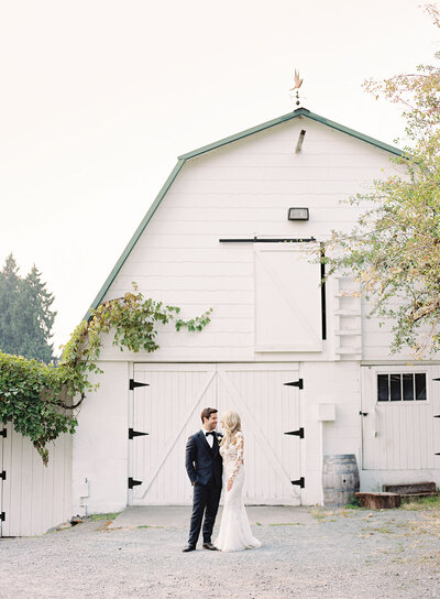 classic white barn as a picturesque backdrop, highlighting a couple's intimate moment in their wedding attire