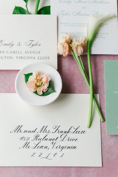 Flatlay of a green and white wedding invitation suite with floral accents.