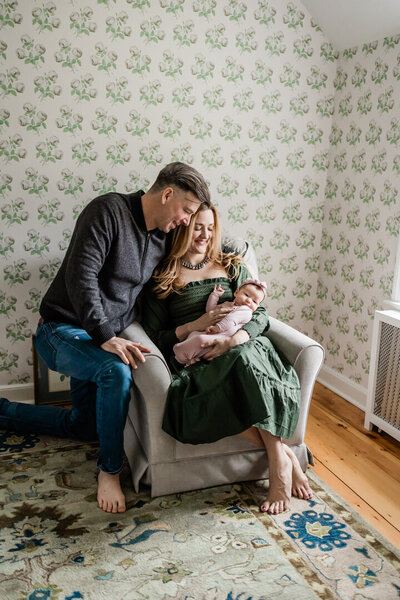 A woman sitting in a chair and holding her baby girl while a man smiles at her