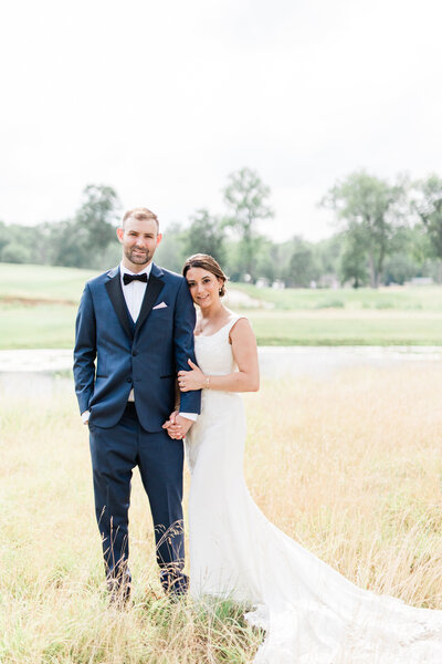 Bride and groom standing next to each other with bride holding on to groom's arm wearing wedding dress