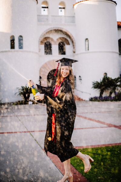 Senior photographer, a girl poses in cap and gown with exploding champagne