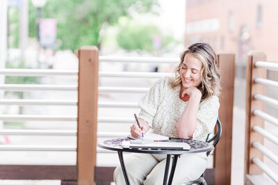 Licensed online therapist Lindsey McKeirnan writes in her planning notebook at one of Charlotte NC's favorite outdoor cafe spots during lifestyle branding session with Amanda Richardson