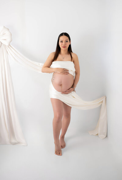 Expectant mother showcasing her bump, wrapped in an off white silky fabric for her maternity pictures in Chicago, IL.
