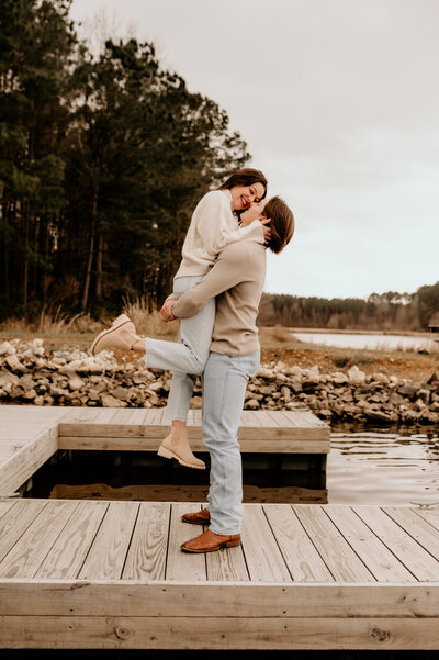 outdoor engagement photos in little rock ar with man picking up woman as they stand on a pier together for their outdoor engagement session