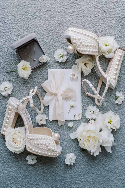 Fine art flatlay with pearl bridal shoes, necklace, rings and white flowers, styled for a wedding near Toronto