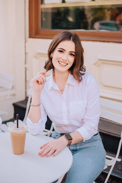 Madison sitting at a table outside with iced coffee smiling
