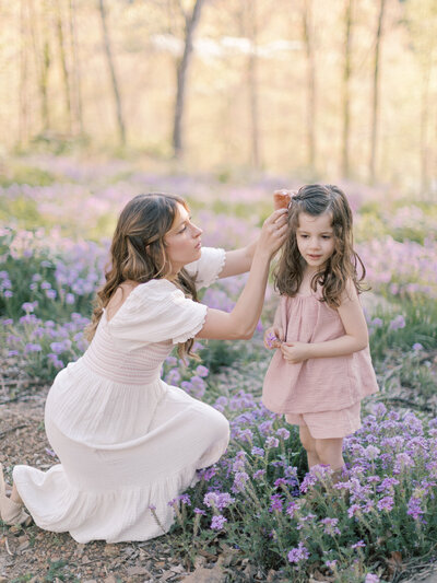 Little Rock photographer Bailey Feeler crouches down in a field of purple flowers while fixing brunette daughter's hair