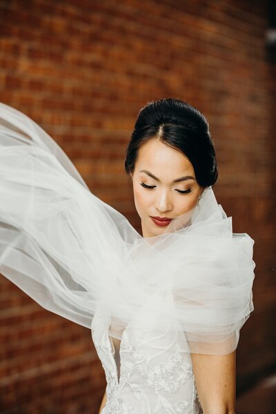 Bride in modern tulle gown posing gracefully against a rustic brick wall.