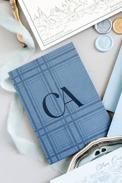 A preppy and tailored wedding itinerary booklet designed by Grey Cove Designs featuring navy plaid pattern, monogram, and soft blue ribbons for a refined paper suite.