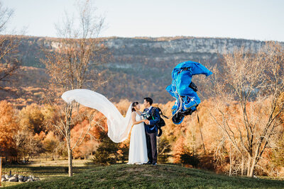 Bride and groom kiss on mountaintop as wedding veil and parachute blow in the wind