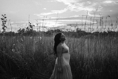 Woman standing in tall grass with a sunset sky in the background. Black and white photo.