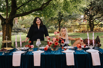 A woman wearing a shirt that says Birdie June sets a plate on a table with candles and flowers, representing wedding management services. 