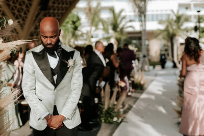 Garza Blanca groom stands with hands held together in silver and black suit