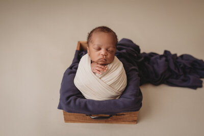Newborn photos with Atlanta, Georgia newborn photographer. Baby boy at his newborn portrait session at marietta ga newborn photography studio propped up in a newborn potato pose wrapped in a cream swaddle