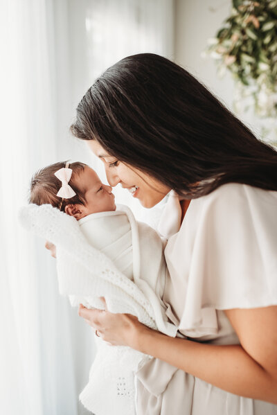 profile view of mom touching noses with newborn in her hands