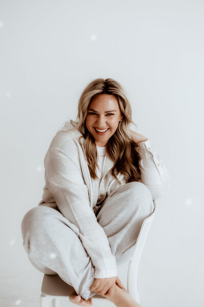 photographer in all white on an all white backdrop laughs while sitting cross legged