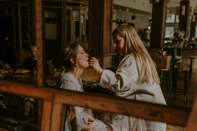 bride getting her makeup done in the reflection of the mirror