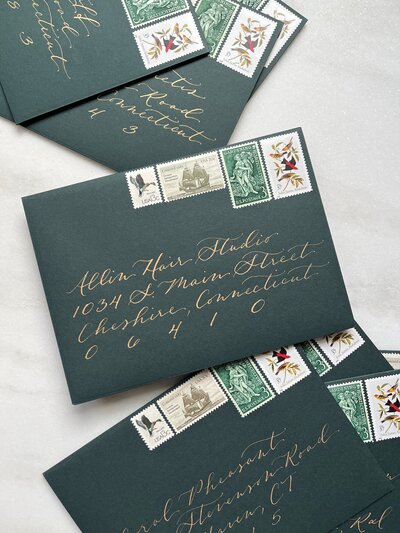 Racing green envelopes with gold calligraphy and vintage postage stamps