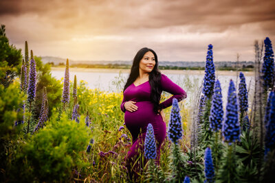 Maternity photographer, a woman poses against a floral backdrop in a beige gown