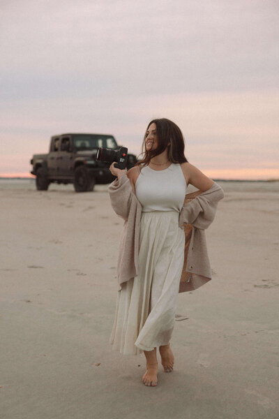marissa a business coach for photographers standing on a beach holding a camera