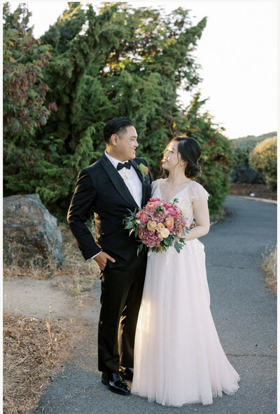 Bride and groom smiling with a vibrant pink and peach bouquet