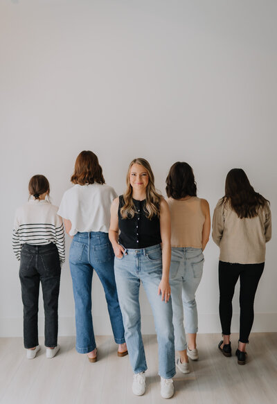 Megan standing and smiling at the camera while her team members stand next to her facing the wall