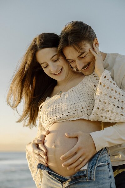 couple laughs during maternity photos on beach