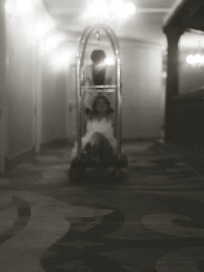 A person pushing their partner on a luggage cart in a hotel.