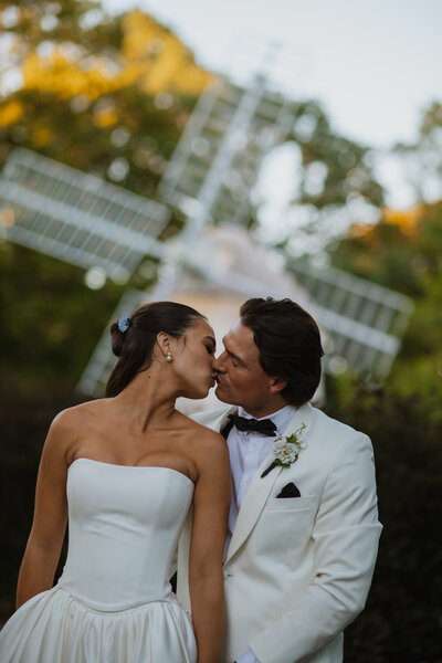 Couple kissing in front of windmill during wedding at Heritage Museum and Gardens