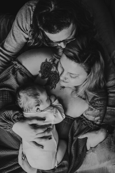 Black and white newborn photo of new mom leaning back on dad with baby laying on mom's chest.