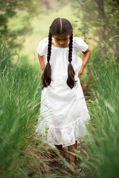 Little girl holding up her dress while walking through a shallow creek in the springtime in kamloops. Captured by Brittany Danielle Photography.
