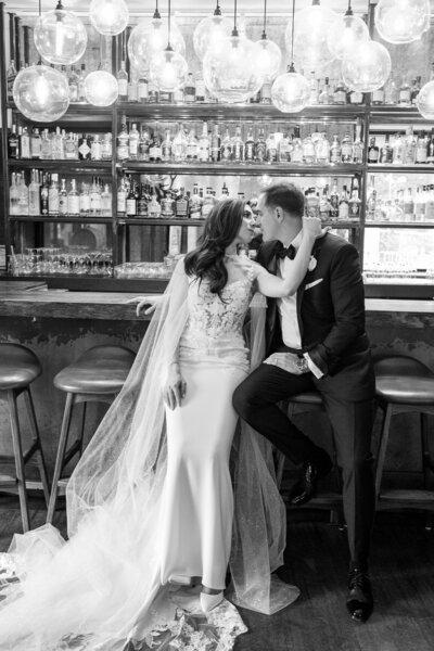 Black and white image of bride and groom sitting on stools at a bar