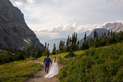 A bride and groom walk along a dirt path in Glacier National Park Montana on their elopement day