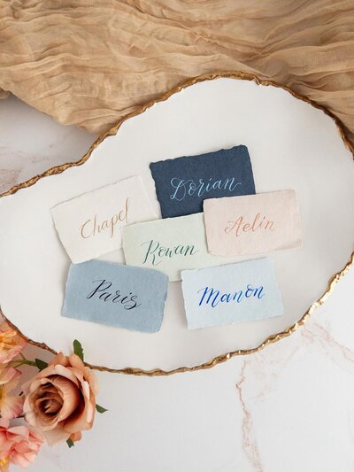colorful handwritten calligraphy wedding place cards with names written in colorful ink, laid on decorative plate